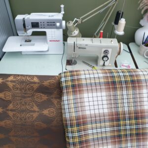 Brown patterned silk fabric sat next to brown checkered fabric, in front of two sewing machines labeled with Bernina