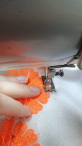 White fabric , with orange flowers , being sewn on a sewing machine